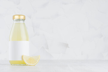 Organic yellow lemon juice in glass bottle mock up with blank label, fruit slice on white wood...
