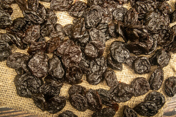 Dried prunes in bulk on burlap with a rough texture. Close up.
