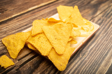 Corn chips with cheese sauce on a wooden background. Close up.