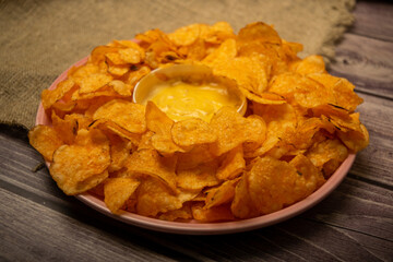 Potato chips on a round platter and a saucepan with cheese sauce. Close up.