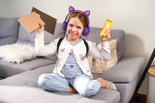 Little girl musical headphones got ready to go to school. Schoolgirl with a backpack, books and a snack for the school day. Education, learning concept. Happy child . Free space for text