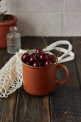 Fresh cherry  in the ceramic cup on the dark brown wooden background