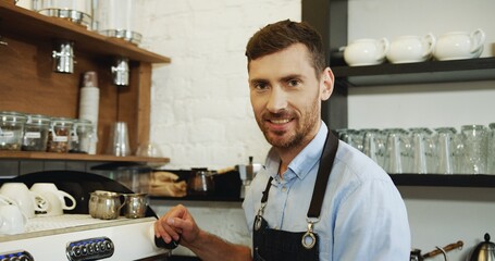 Portrait of the handsome waiter making coffee at the special coffee machine and smiling to the camera. Close up.