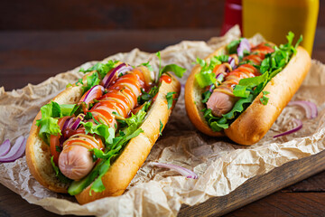 Homemade hot dog with sausage, salad, carrot, cucumber and tomato on wooden background