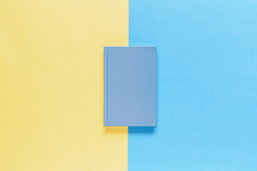 Closed blue notebook on yellow and blue background. Top view, mockup
