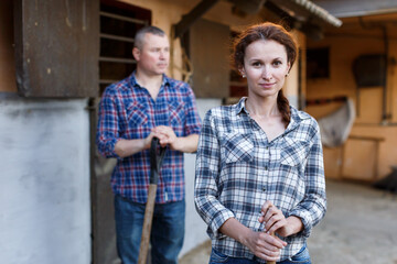 Mature positive family couple with tools standing at stabling outdoor