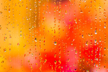 Jewel like drops of rainwater on the outside of a windowpane with vibrant autumn coloured leaves  providing a soft defocussed background.