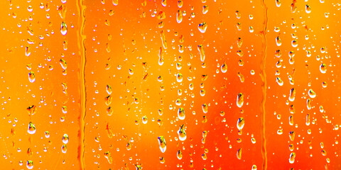 Jewel like drops of rainwater on the outside of a windowpane with vibrant autumn coloured leaves  providing a soft defocussed background.