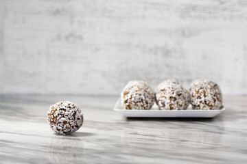 Homemade energy balls with dried apricots, raisins, dates, prunes, walnuts and coconut. Healthy sweet food. Energy balls in a plate on a marble gray background. Close up. Side view. Copy space