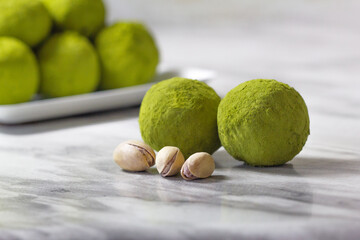 Homemade energy balls with dried apricots, raisins, dates, prunes, walnuts, pistachios and green matcha. Healthy sweet food. Energy balls in a plate on a marble grey background. Close up. Side view.
