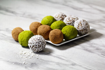 Homemade energy balls with dried apricots, raisins, dates, prunes, walnuts, pistachios, green matcha, cacao and coconut. Assortment. Healthy sweet food. Energy balls on a marble grey background.