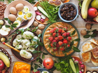 Fragment of a table with vegetarian simple healthy food, cake with strawberries, breadcrumbs, potatoes, egg, herbs. Festive rustic table.