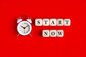 The word start now is written on wooden blocks with an alarm clock. Timing, motivation, strategy and action concept.