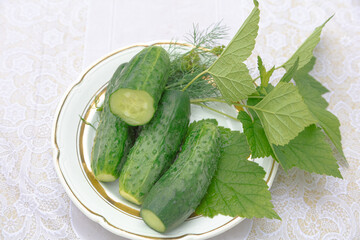 Freshly pickled cucumbers on a plate and currant leaves on a light background.