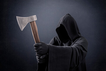 Scary figure in hooded cloak with axe in the dark