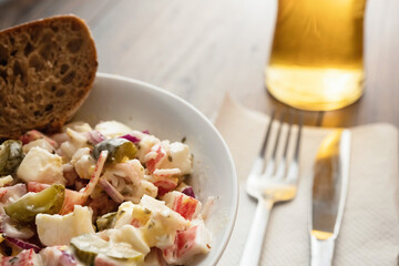 Crab stick salad in focus, Glass with lager beer, fork and knife out of focus. Restaurant food concept.