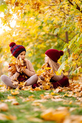 girls in the hat sit in autumn Park with maple leaf  and play, have fun.