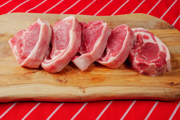 Five fresh raw lamb loin chops on a wooden cutting board and traditional butcher red and white...