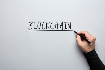 Obraz na płótnie Canvas The word blockchain handwritten with a male hand on grey background. Concept of blockchain technology.