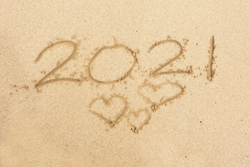 Hand written sign on a sand 2021 and three heart shape symbol of love.