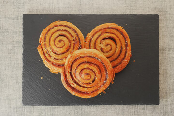 Three freshly cooked cinnamon swirls served on a stone plate. Top view.