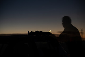 Silhouette of a person on a car in dark night with  cameras utensils on the roof