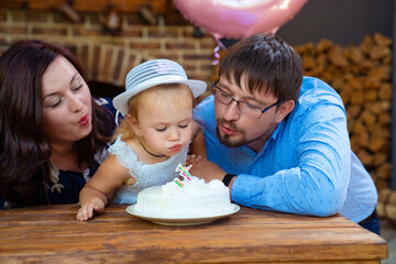 Fototapeta premium parents with daughter blowing out candle on cake.