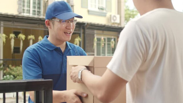 Young postal delivery courier man holding parcel boxes for sending to customer, Asian men signing and pay via qr code on mobile phone for receive delivered parcels outdoors.