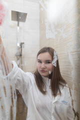A young slender girl in a man's shirt is standing in the shower stall