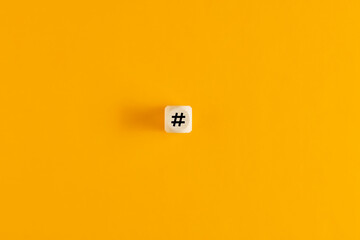 Hashtag symbol on wooden cube against yellow background. Overhead view with copy space.