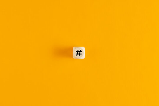 Hashtag symbol on wooden cube against yellow background. Overhead view with copy space.