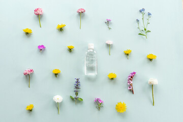 Floral pattern on blue, summer concept. Leaves and little meadow flowers. Clear bottle with lotion in the center.