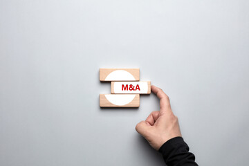 M&A merger and acquisitions concept. Male human hand pushing the wooden block with the word M&A and...