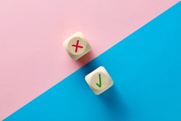 Wrong and right symbols on wooden cubes on pink and blue background.