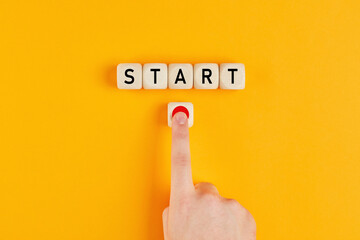 The word start on wooden cubes with a male hand pressing the start button. To make a new start in life, business, education or career concept. - obrazy, fototapety, plakaty
