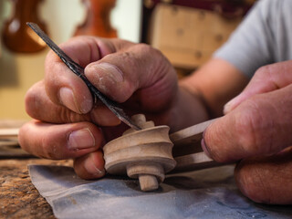 Hands of luthier violin maker carving and working on a instrument scroll in his workshop in Cremona, Italy