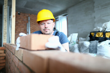 Low angle of male professional in yellow hard hat building wall inside new empty apartment