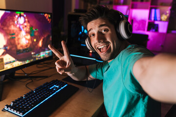 Image of man gesturing peace sign and taking selfie while playing game © Drobot Dean