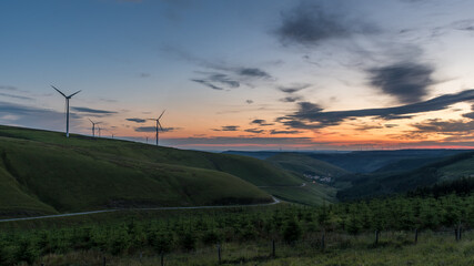 Fototapeta na wymiar Sunset over the south Wales valleys from the Bwlch mountain. A road winds around the hillside to the village of Abergwynfi. The hillside has a wind farm on it. 