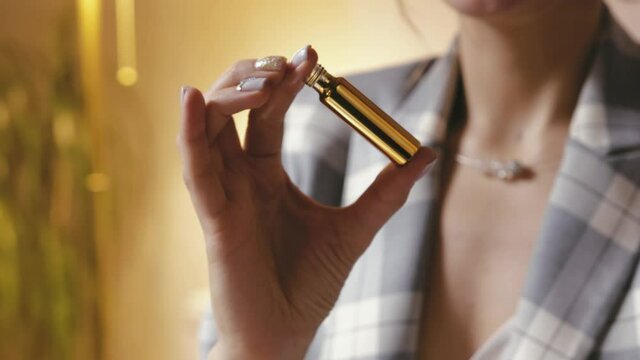 Close-up of a woman's hands mixing perfume ingredients in a Golden test tube. The perfumer prepares Cologne in the workshop, shakes essential oils in a container. The concept of a micro business