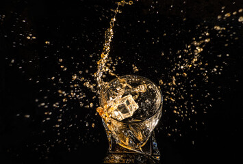 A glass of whiskey with splashes from the ice cube over black background. alcohol splashes. whisky or cognac or another type of alcohol with splashes.