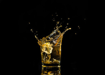 A glass of whiskey with splashes from the ice cube over black background. alcohol splashes. whisky or cognac or another type of alcohol with splashes.