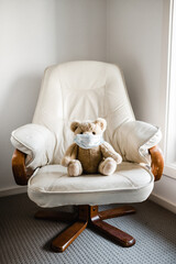 A child's teddy bear sitting on a chair wearing a facemask
