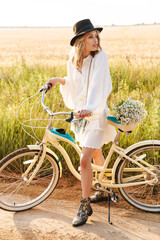 Fototapeta na wymiar Image of young woman holding flowers and riding bicycle in countryside