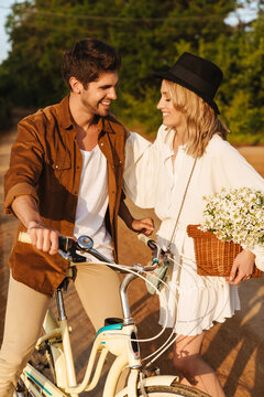 Image of caucasian couple smiling and riding bicycle in countryside