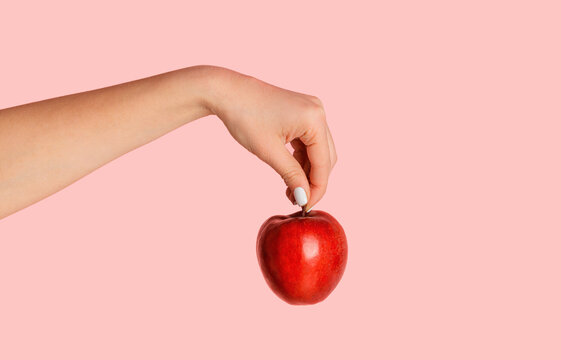 Millennial girl holding yummy red apple over pink background, closeup