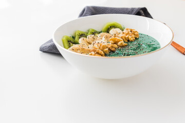 spirulina smoothie bowl with banana, walnuts, kiwi and chia seeds on white background