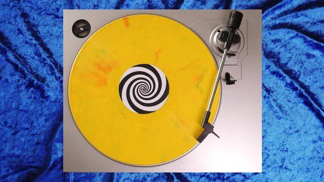 Yellow, green & red splatter 12&rdquo; vinyl record on a DJ turntable with blue velvet background. Circular long player shot from above. Party, disco, punk, grunge, pop, VJ. 60s, 70s, 80s, 90s 4K