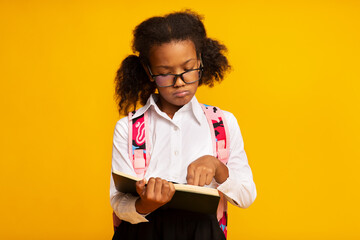 Dyslexic Schoolgirl Reading Book Standing Over Yellow Background, Studio Shot - obrazy, fototapety, plakaty