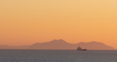 Naklejka na ściany i meble cargo ship crossing the sea at sunset
